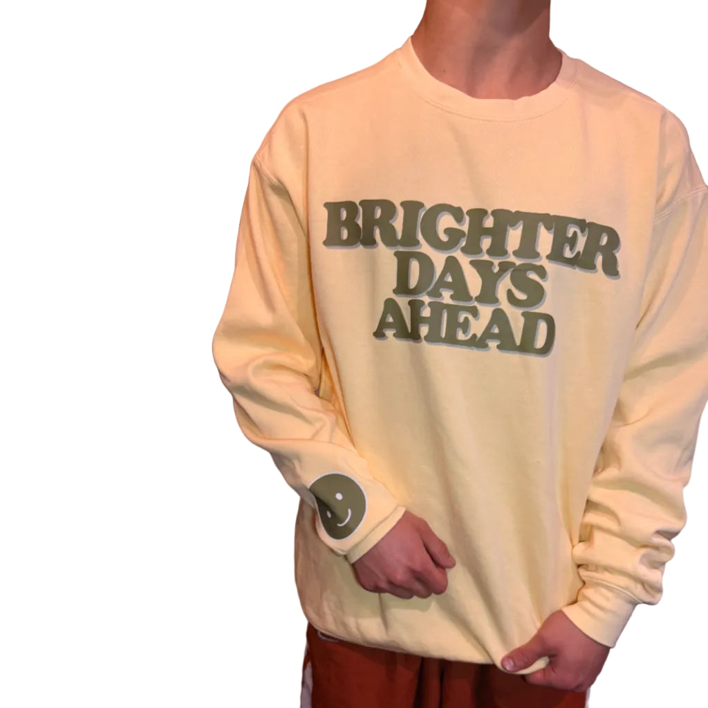 Person holding a light-colored sweatshirt with 'BRIGHTER DAYS AHEAD' text.
