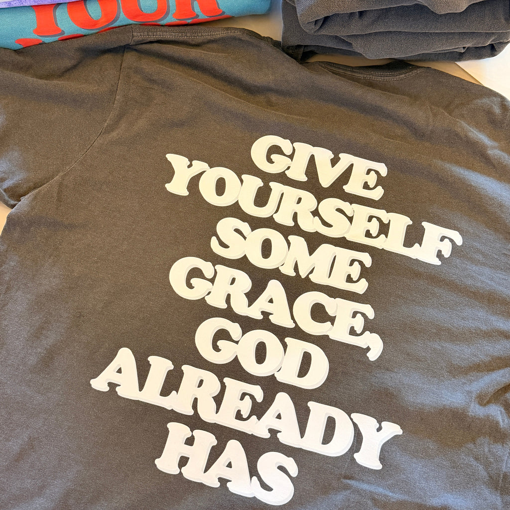 Gray t-shirt with motivational text on a pile of folded clothes.