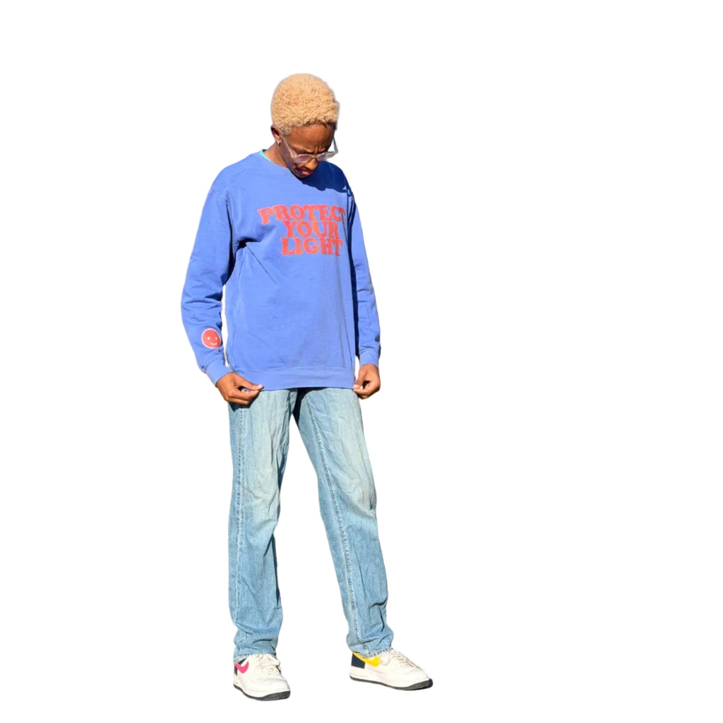 Person wearing a blue sweatshirt with red text and light blue jeans standing on a sidewalk in front of a house.