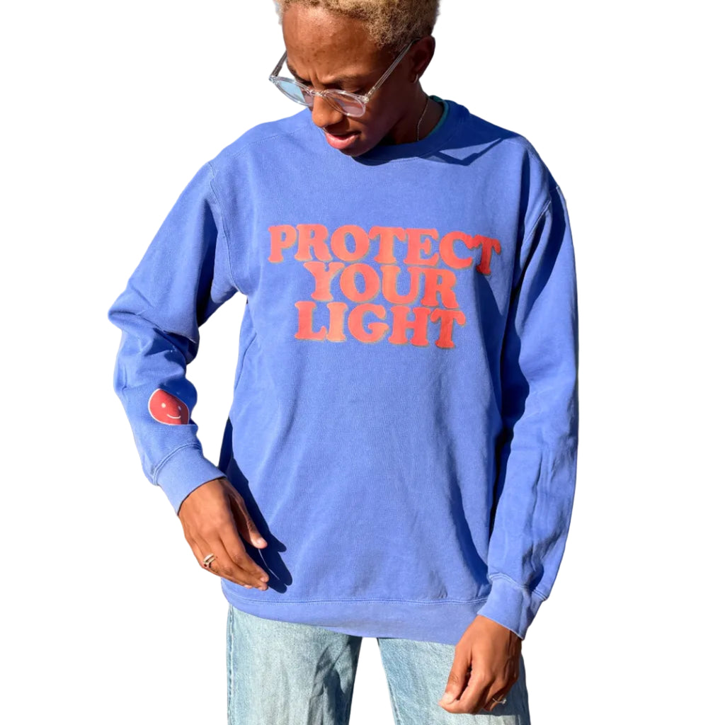Person wearing a blue sweatshirt with 'Protect Your Light' text in an outdoor setting