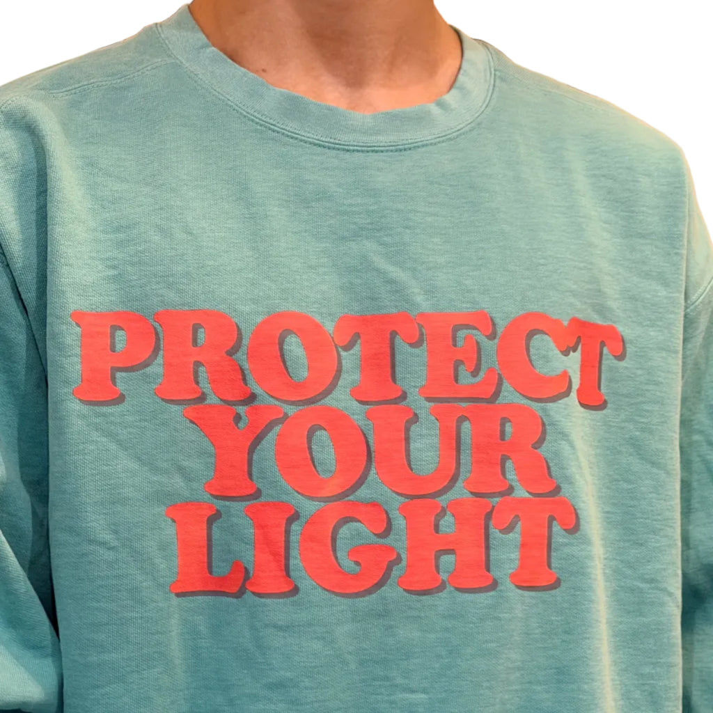 Light blue shirt with red text 'PROTECT YOUR LIGHT' held by a person.