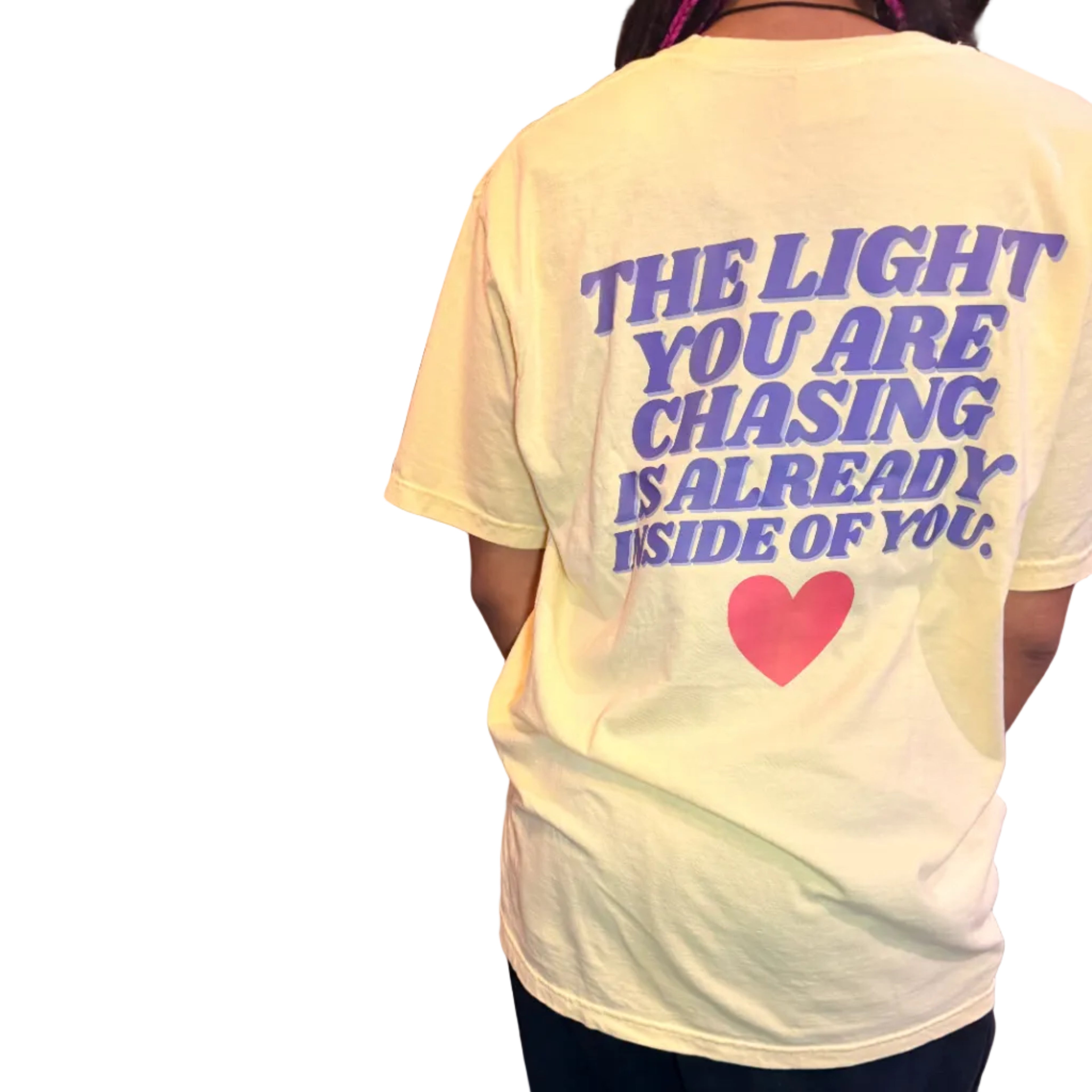 Person wearing a light yellow t-shirt with text and a heart graphic, standing indoors.