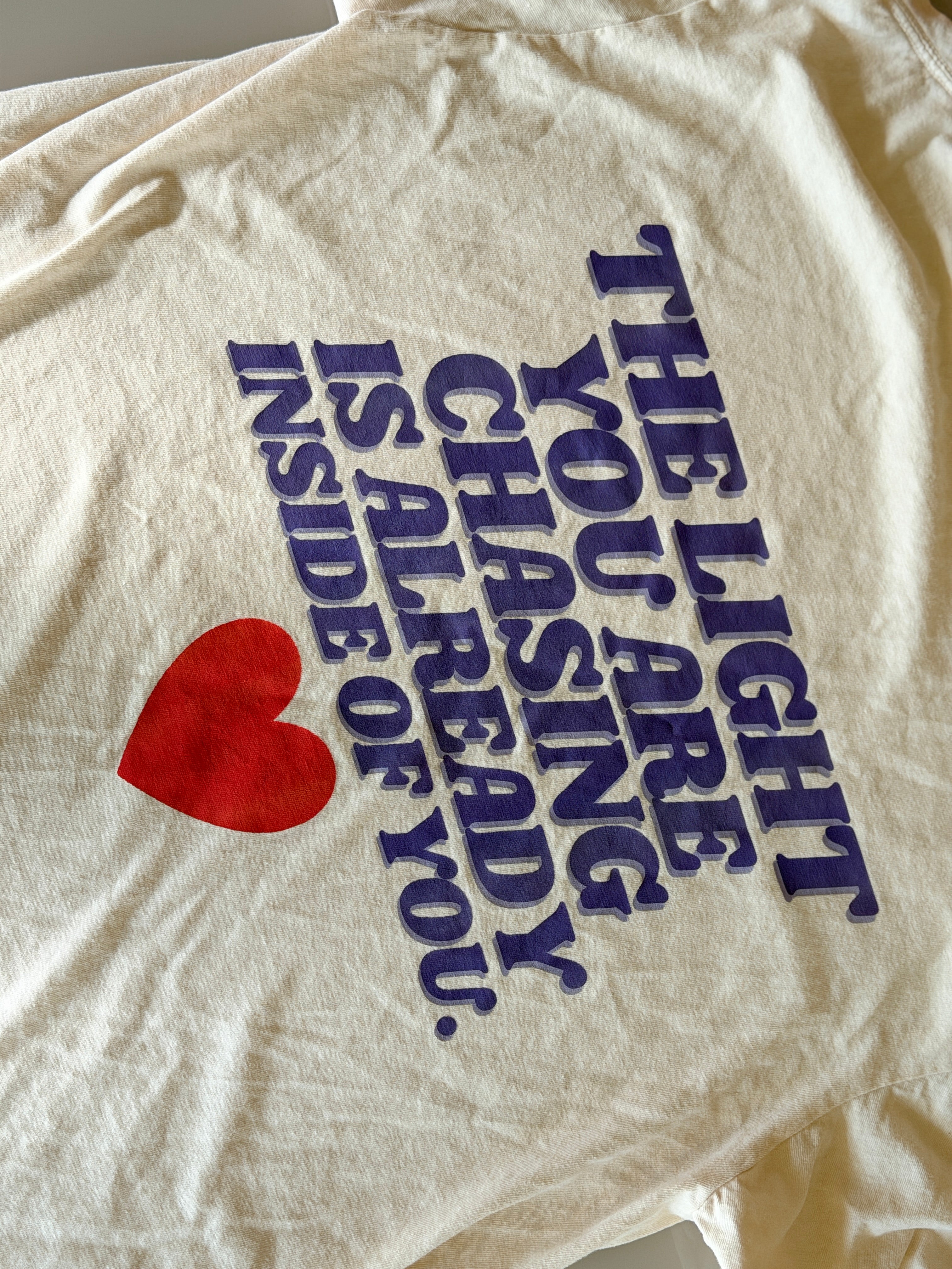 White t-shirt with motivational quote and red heart on a plain background