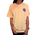 Person holding a light-colored shirt with a small logo on a dark surface