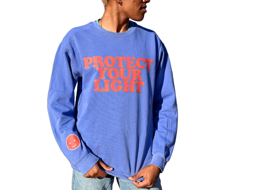 Person wearing a blue long-sleeve shirt with 'PROTECT YOUR LIGHT' text in red outdoors.