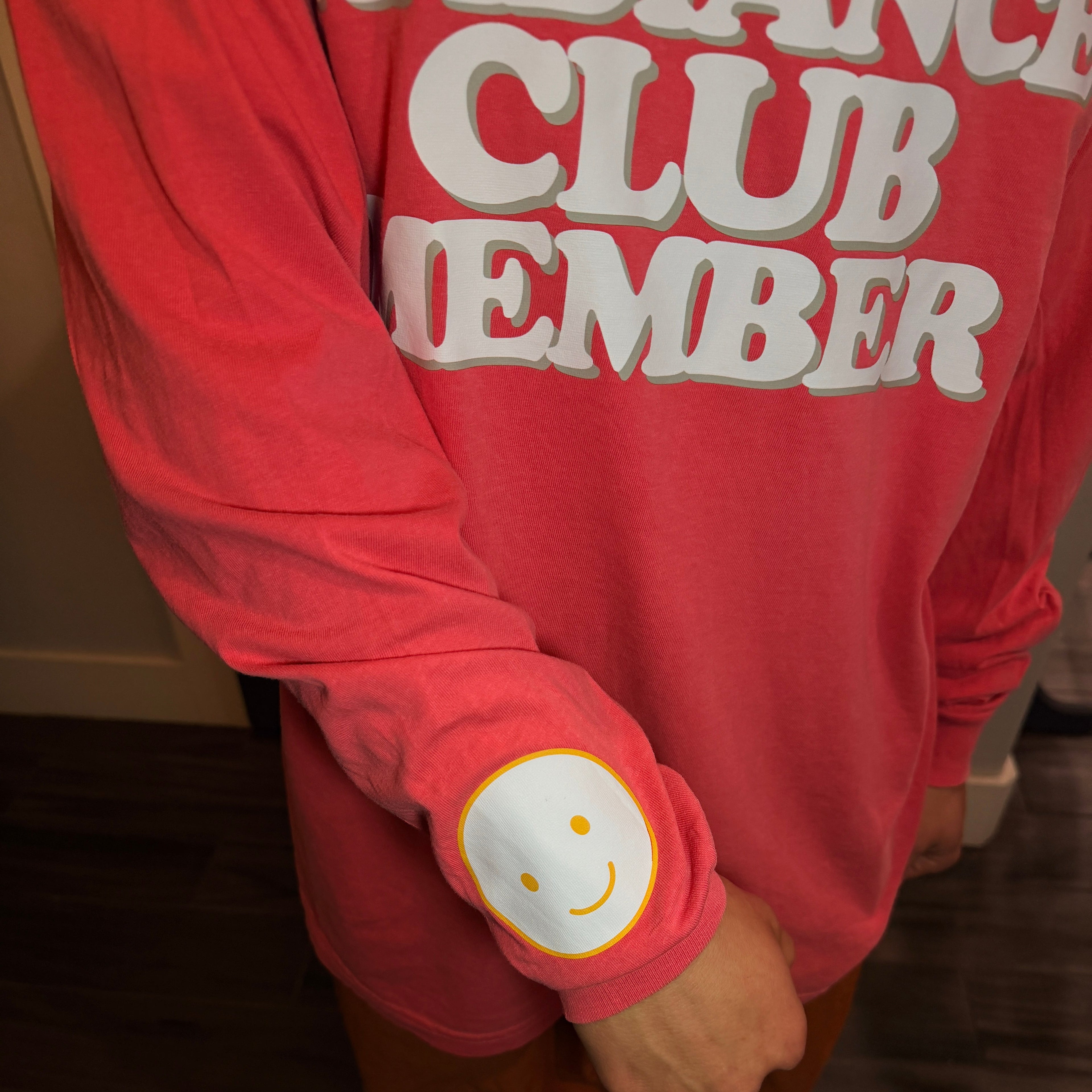 Red sweatshirt with 'CLUB MEMBER' text and a smiley face design on a dark background