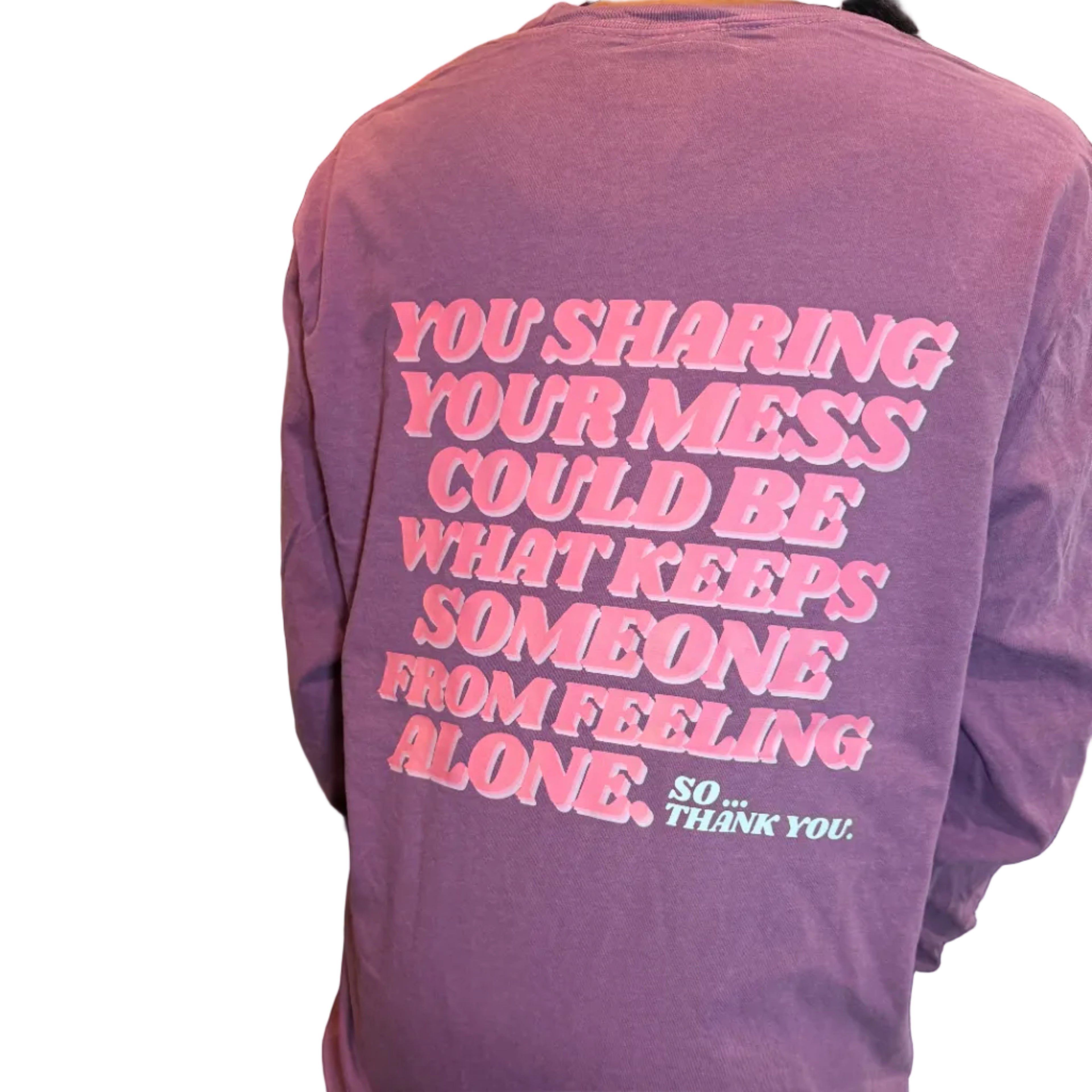 Purple t-shirt with pink text worn by a person, with a blurred background.