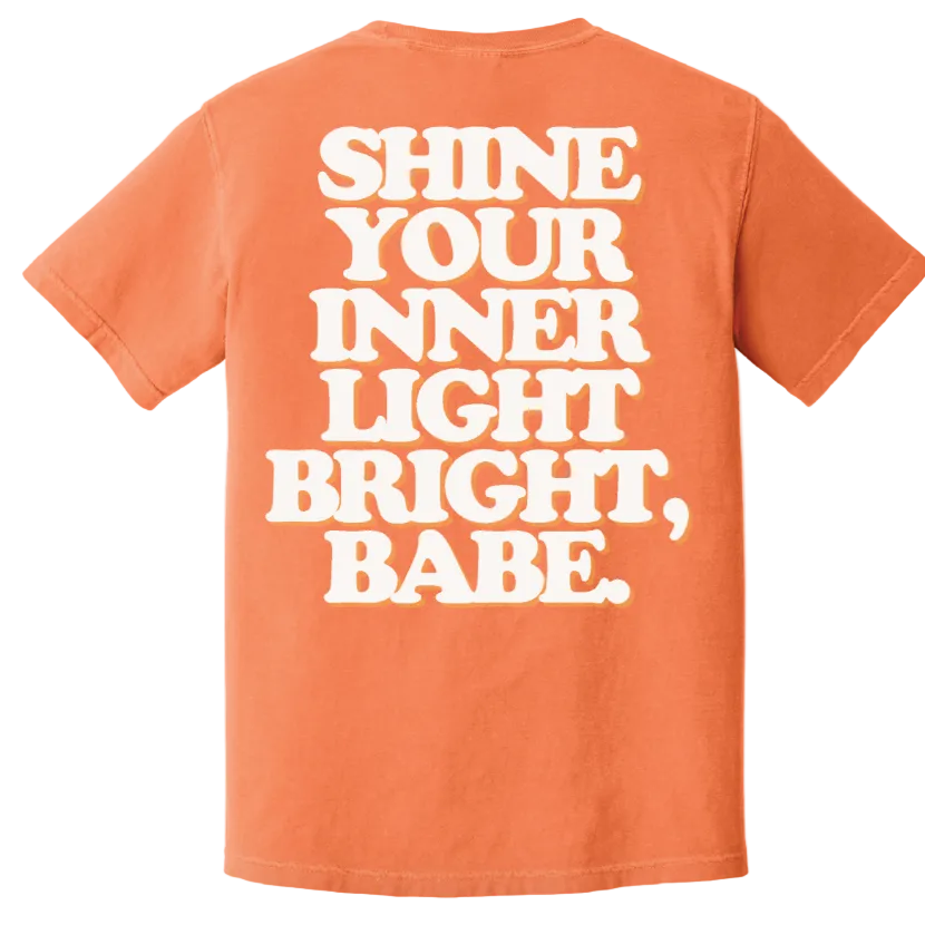 Orange t-shirt with white text 'SHINE YOUR INNER LIGHT BRIGHT, BABE' on a white background