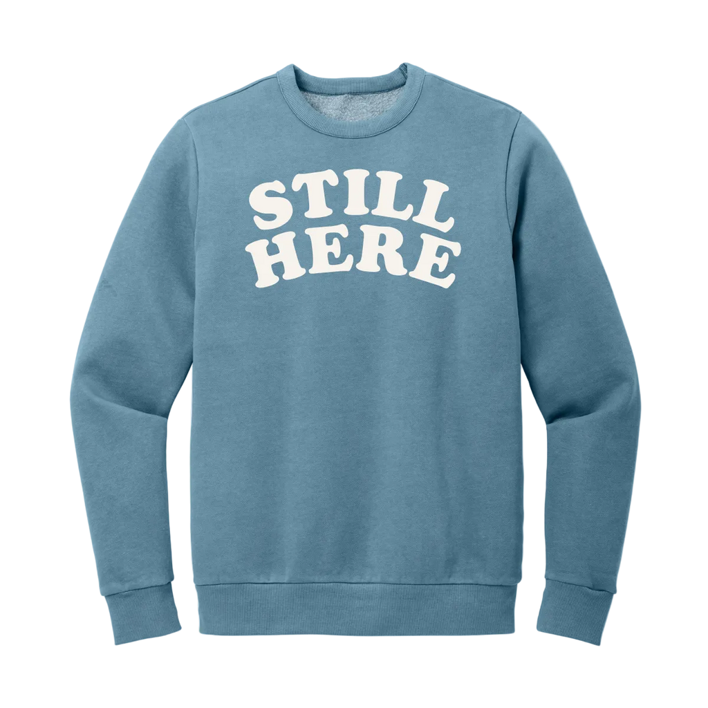 Blue sweatshirt with 'STILL HERE' text on a white background