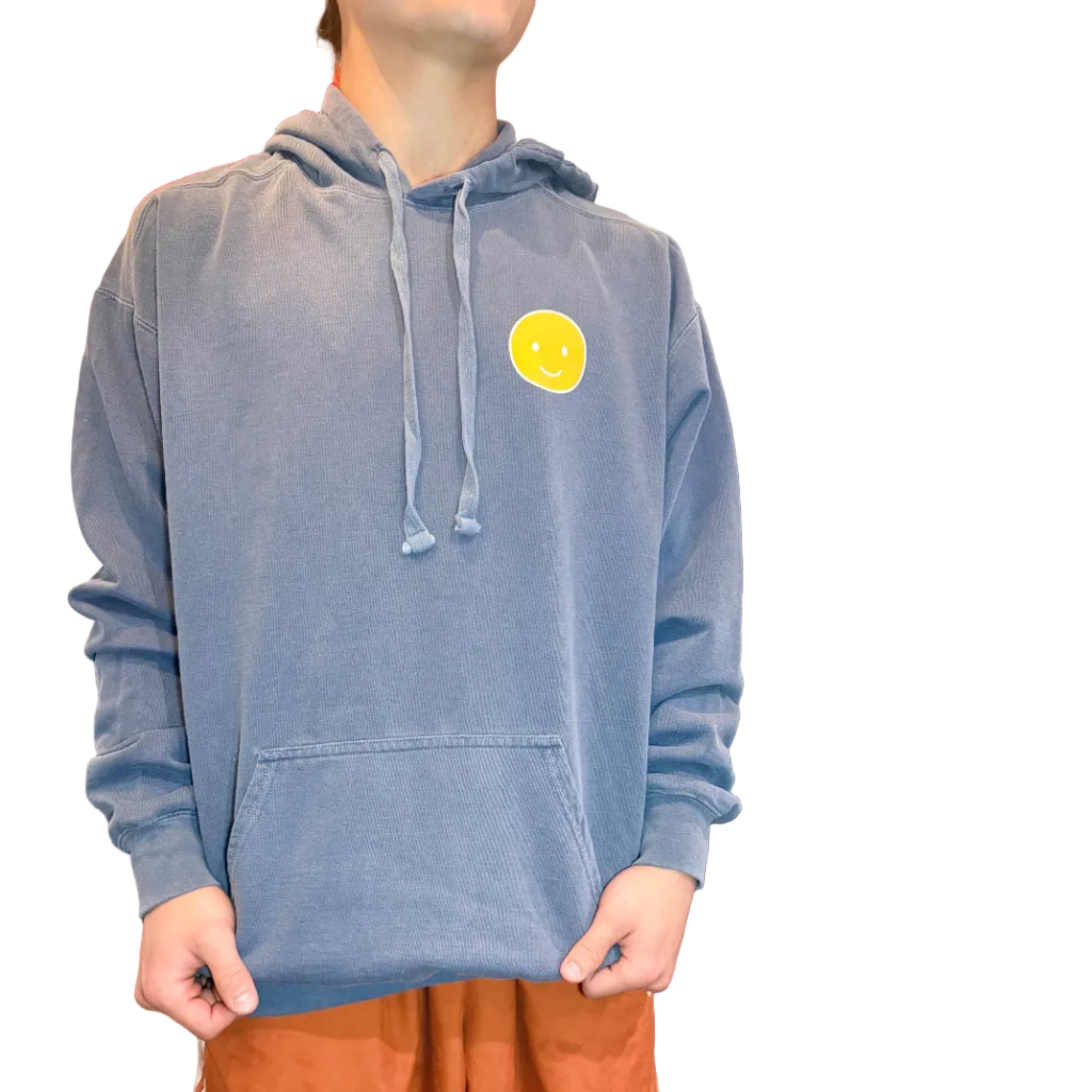Person holding a blue denim jacket with a yellow circle logo in front of a wooden panel wall.