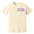 Beige t-shirt with 'one day at a time' text in purple on a white background