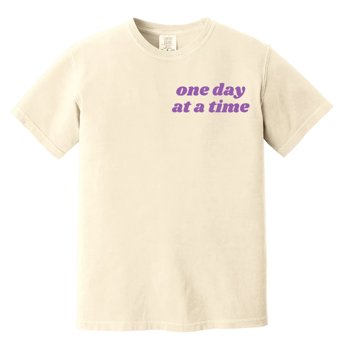 Beige t-shirt with 'one day at a time' text in purple on a white background