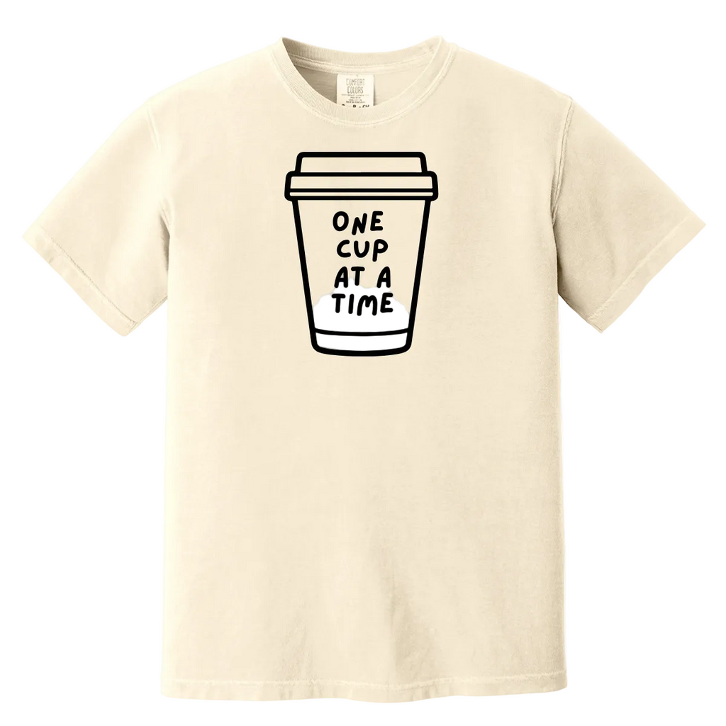 Beige t-shirt with a coffee cup graphic and text 'ONE CUP AT A TIME' on a white background